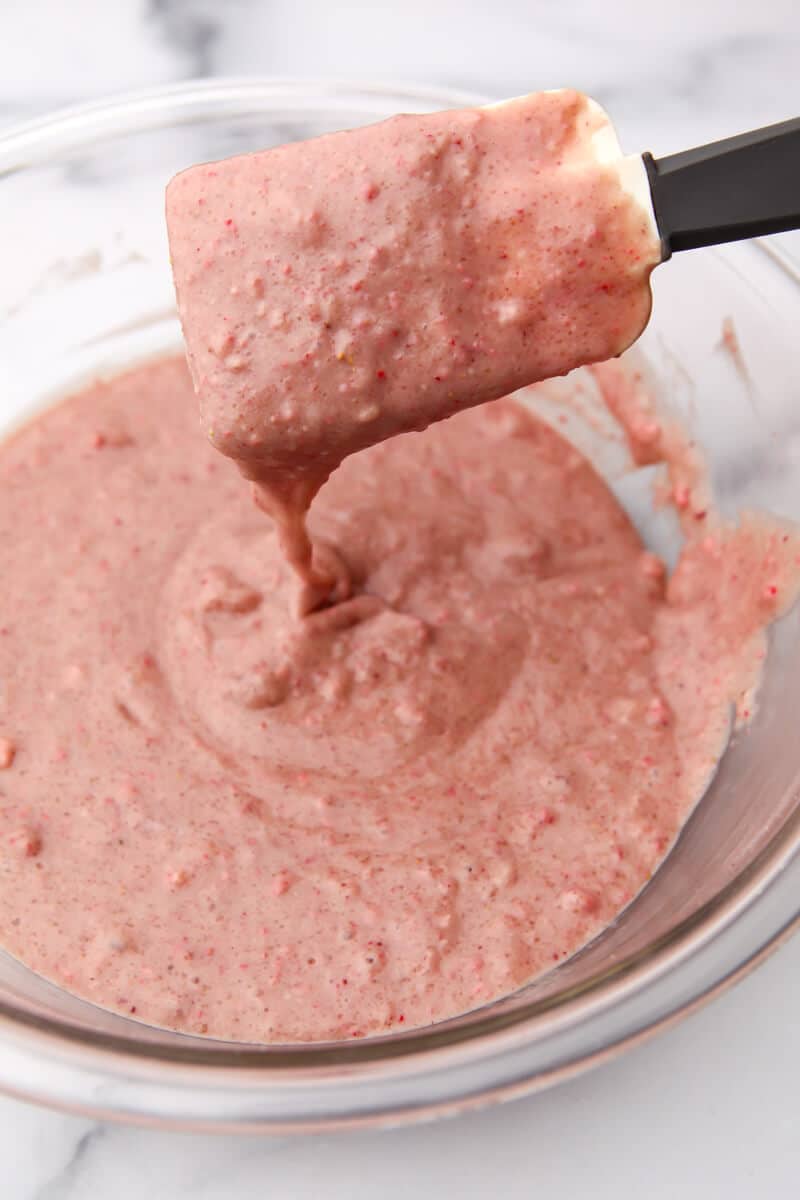 Vegan strawberry cupcake batter in a glass bowl being stirred with a spatula.