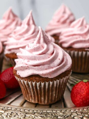 Vegan strawberry cupcakes with strawberry buttercream on a silver tray with some strawberries around.