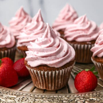 Vegan strawberry cupcakes with strawberry buttercream on a silver tray with some strawberries around.