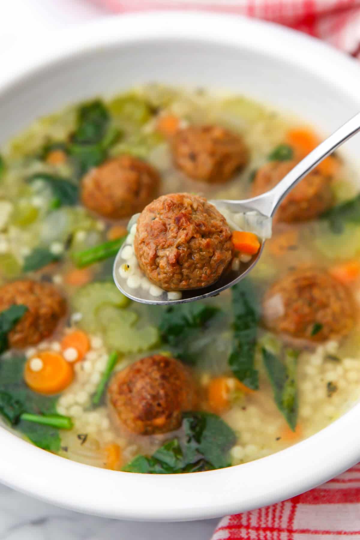 A top view of vegan wedding soup with a meatball in a spoon over the bowl of soup.