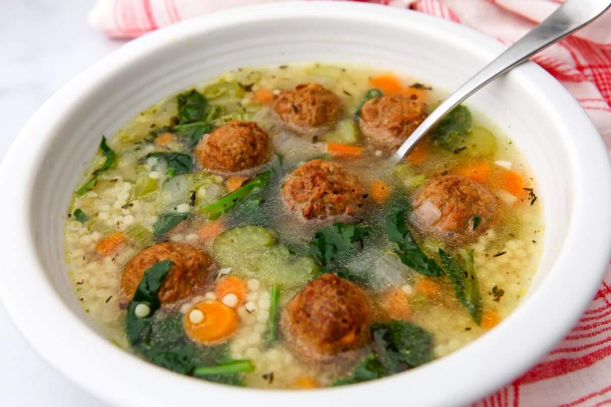 Vegan wedding soup in a white bowl filled with veggies and meatballs.