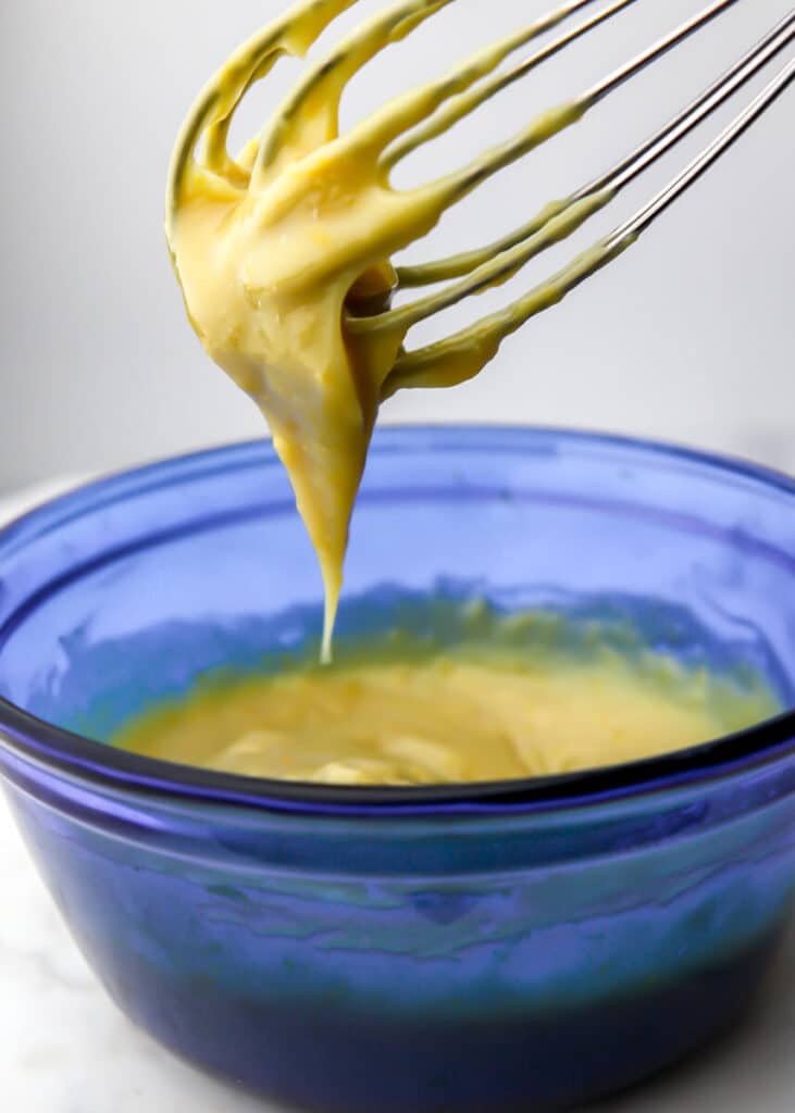 A blue bowl filled with vegan pastry cream with a whisk above it with custard on the whisk.