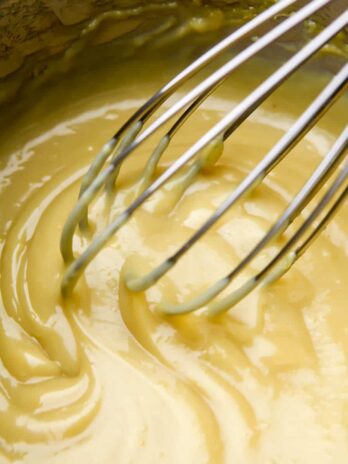 A saucepan full of veg00an custard being stirred with a whisk.