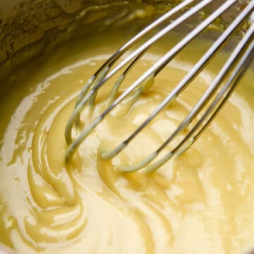 A saucepan full of veg00an custard being stirred with a whisk.