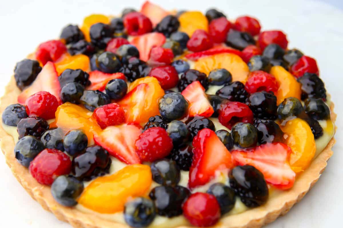 A top view of a vegan custard fruit tart topped with berries and mandrine orange slices.