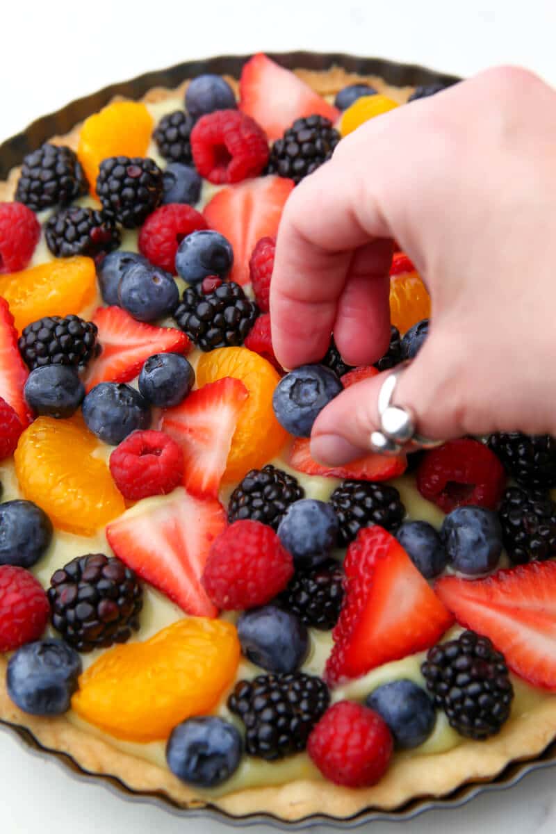 Someone placing berries on a fruit tart.