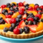 A vegan fruit tart topped with fruit and berries on a blue plate.