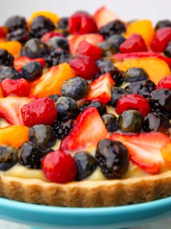 A vegan fruit tart topped with fruit and berries on a blue plate.