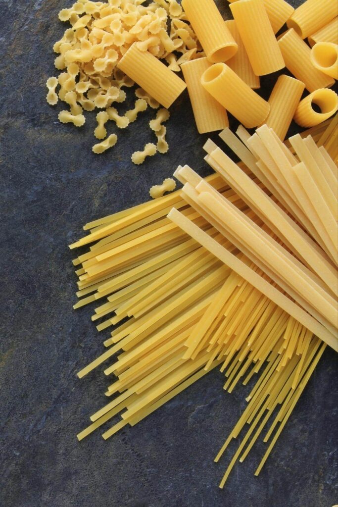 A variety of vegan pasta shapes on a dark gray countertop.