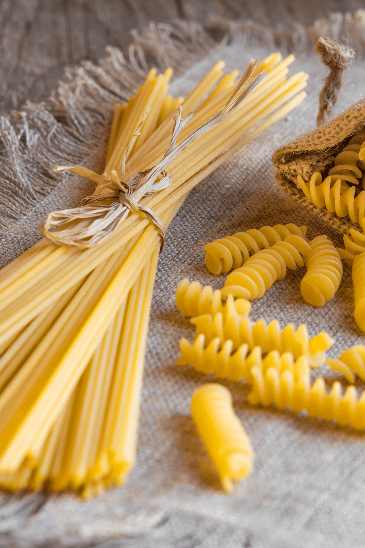Vegan dry pasta in the shape of spaghetti and spirals on a tan tablecloth.