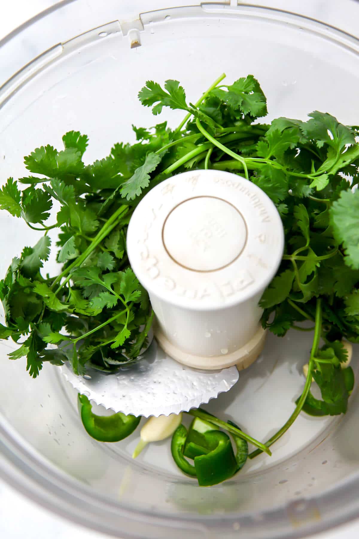 A food processor filled with cilantro, garlic, jalapenos, and lime juice.