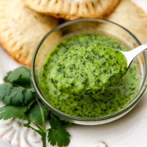 A small clear glass bowl filled with garlic cilanto sauce being scooped out with a spoon.