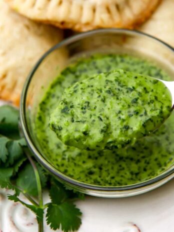 A small clear glass bowl filled with garlic cilanto sauce being scooped out with a spoon.