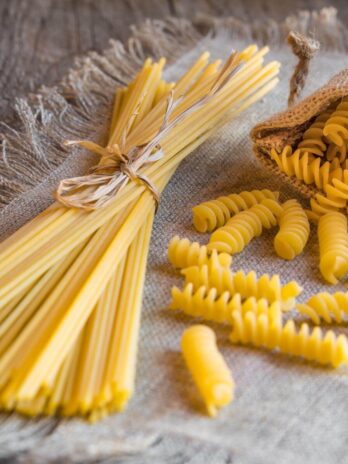 Vegan dry pasta in the shape of spaghetti and spirals on a tan tablecloth.