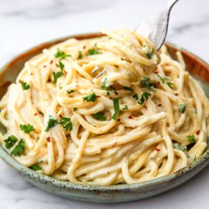 A green plate filled with pasta covered in silken tofu pasta sauce being scooped up with a fork.