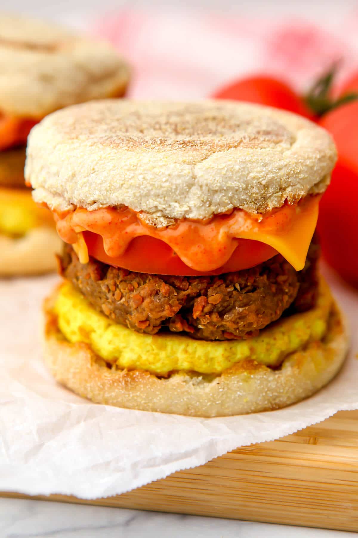 A close up of a vegan breakfast sandwich with tomatoes and a tea towel behind it.