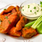 Vegan buffalo chicken wings on a white plate with vegan blue cheese dip and celery on the side.
