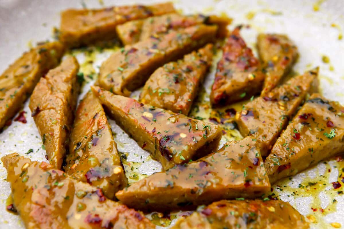 Vegan chicken wings cooking in a pan with vegan honey garlic sauce on them.