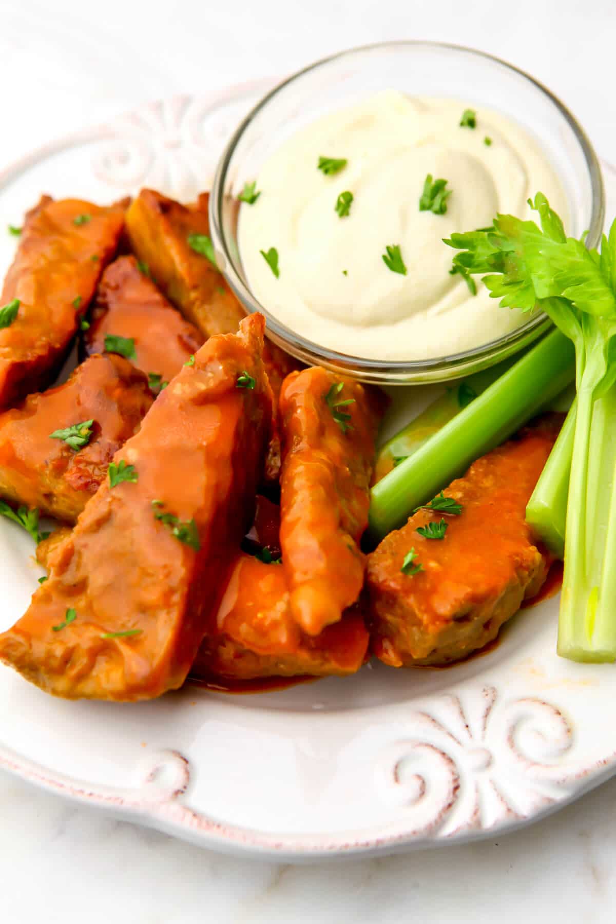 A top view of a plate of vegan chicken wings with buffalo sauce on them and blue cheese dressing and celery on the side.
