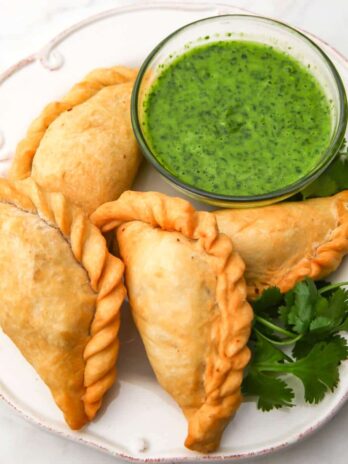 A white plate filled with vegan empanadas and cilantro dipping sauce on the side.