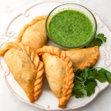 A white plate filled with vegan empanadas and cilantro dipping sauce on the side.