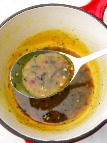 A red saucepan with vegan honey galic sauce being scooped out with a spoon.