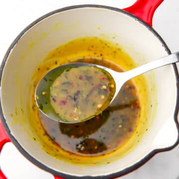 A red saucepan with vegan honey galic sauce being scooped out with a spoon.