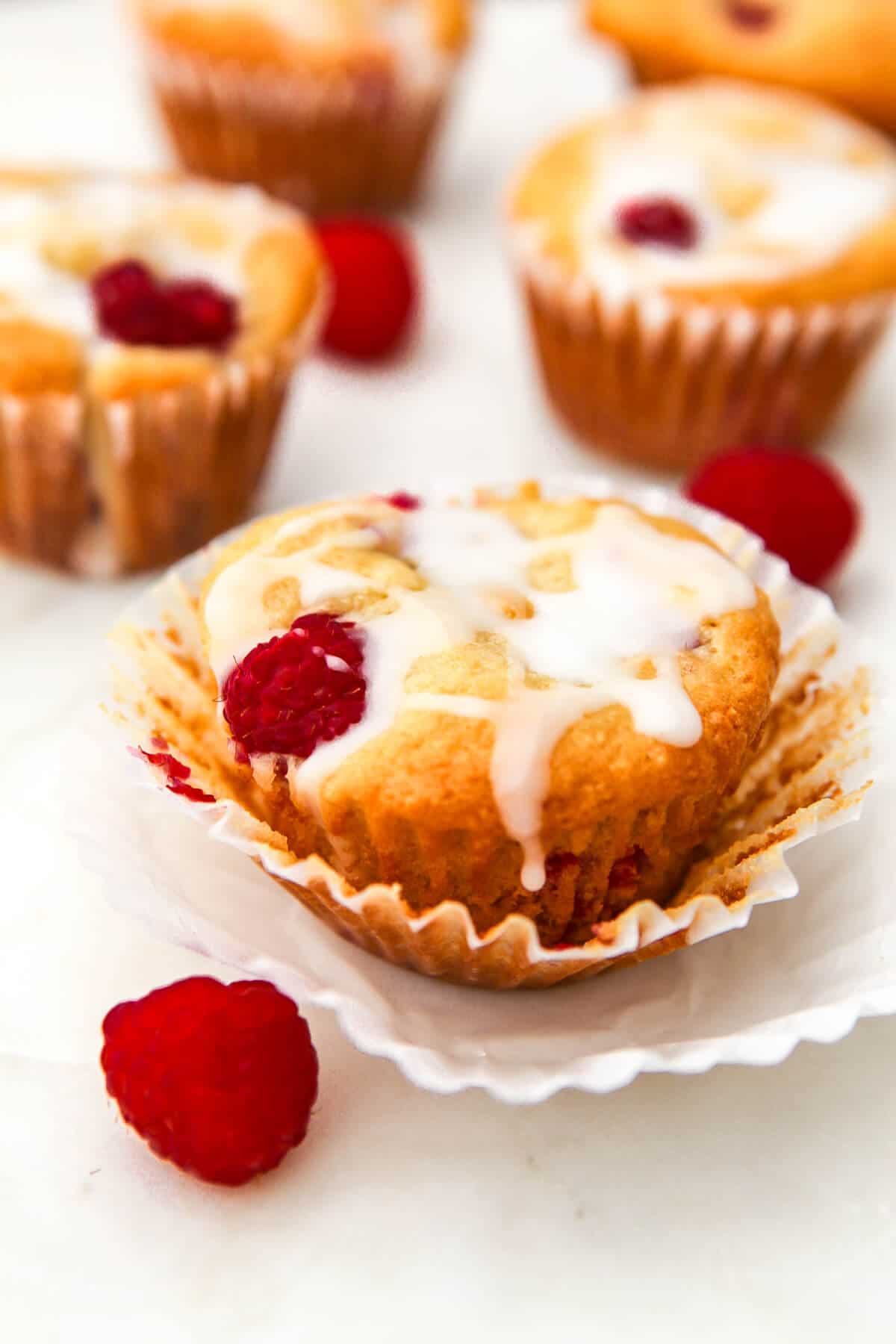 Vegan raspberry muffins on a marble countertop with fresh red raspberries around them.