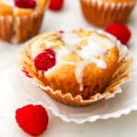 A vegan raspberry muffin with white icing drizzled on top and a raspberry on the side.