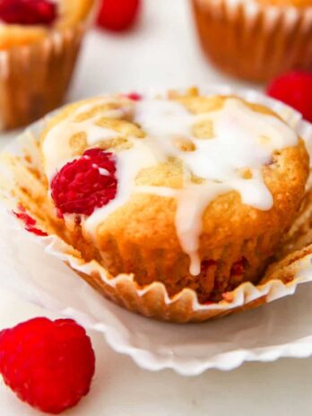 A vegan raspberry muffin with white icing drizzled on top and a raspberry on the side.