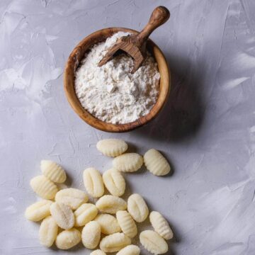 A top view of gnocchi on a blue countertop with a bowl of flour near it.