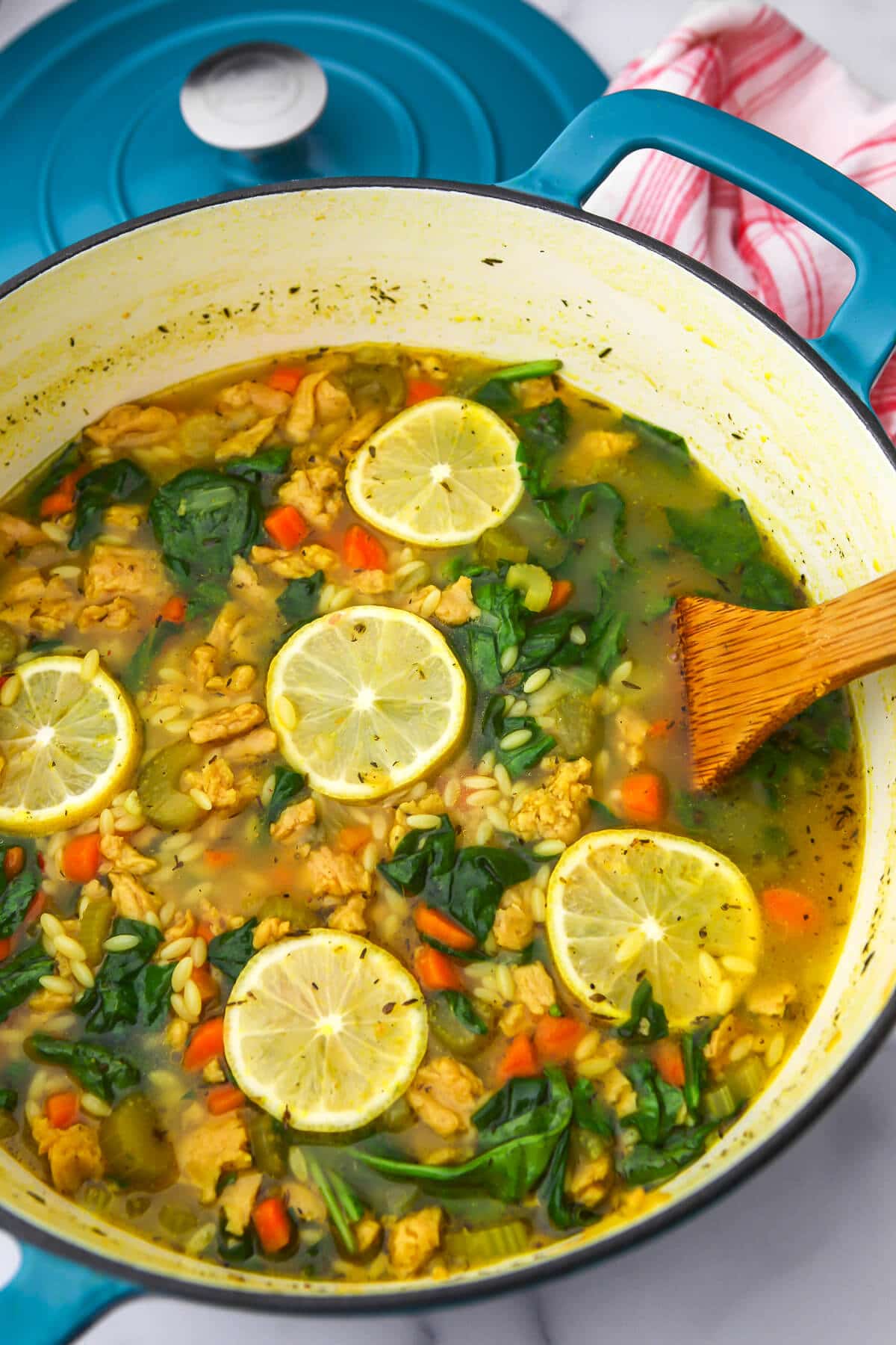 A top view of a blue dutch oven with vegan chicken and orzo soup with lemon and spinach.