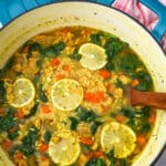 A large pot of vegan orzo soup with spinach and slices of lemon in it.