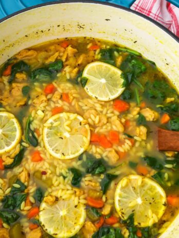 A large pot of vegan orzo soup with spinach and slices of lemon in it.
