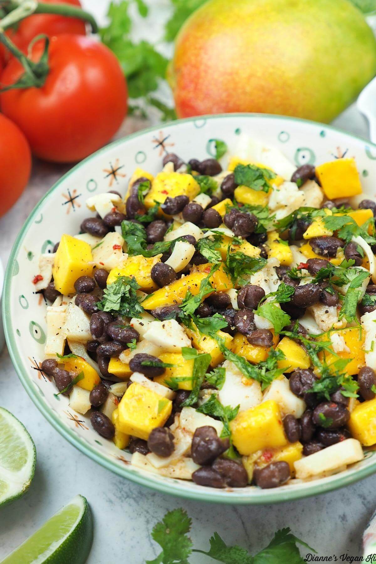 A black bean mango salad in a bowl with tomatoes and mango in the background.