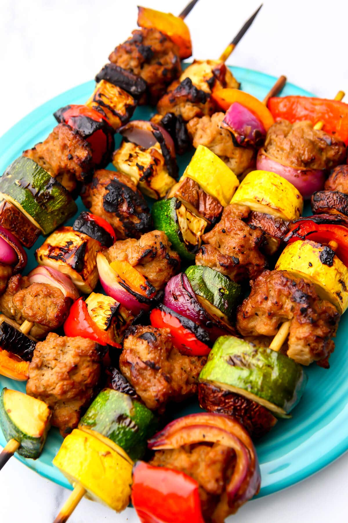 A blue plate filled with colorful vegan kebabs filled with seitan and grilled veggies.