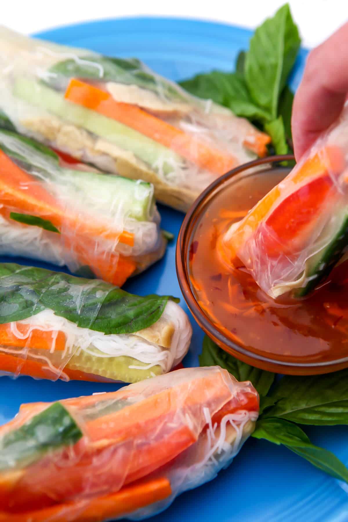 A tofu spring roll being dipped into sweet chili sauce.