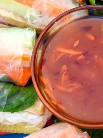 Sweet chili sauce in a glass bowl next to spring rolls.