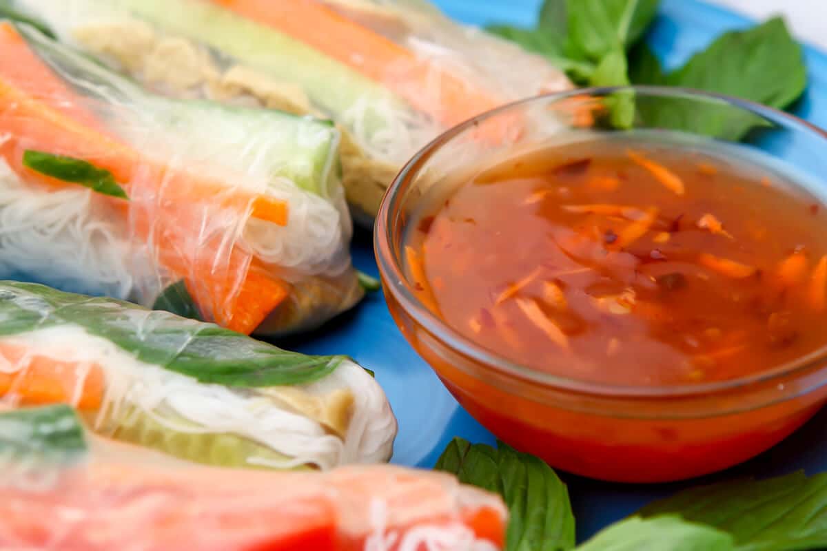 Vegan summer rolls on a blue plate with sweet chili dipping sauce on the side.