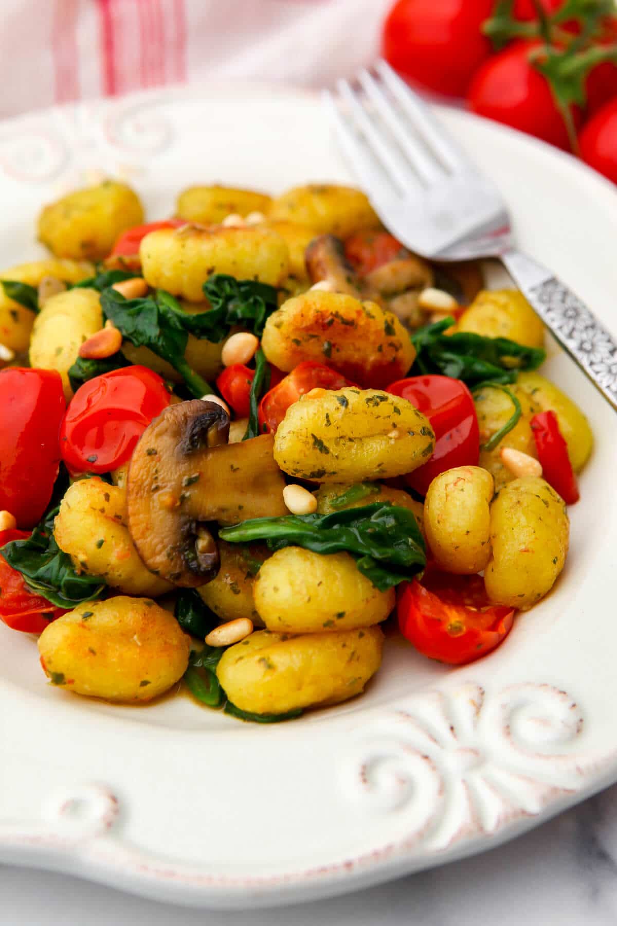 A  white plate full of fried gnocchi and colorful veggies with pine nuts sprinkled on top.