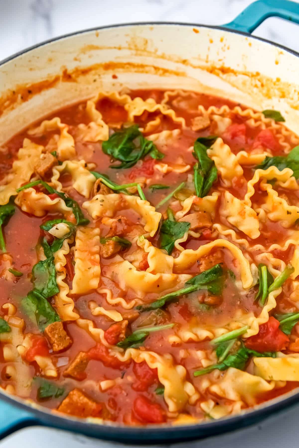 Cooked noodles and spinach in a large pot of vegan lasagna soup.