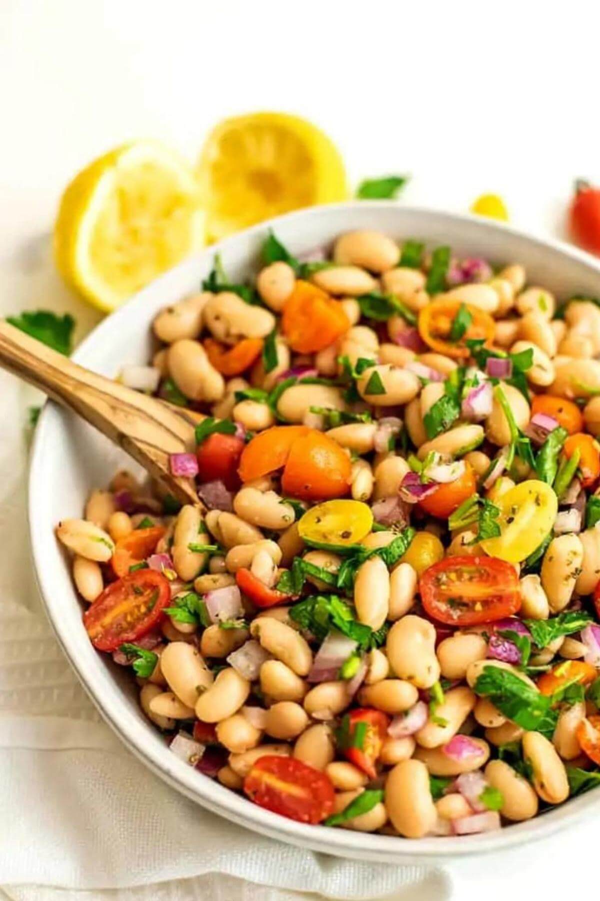 A white bean salad in a large white bowl with lemons in the background.