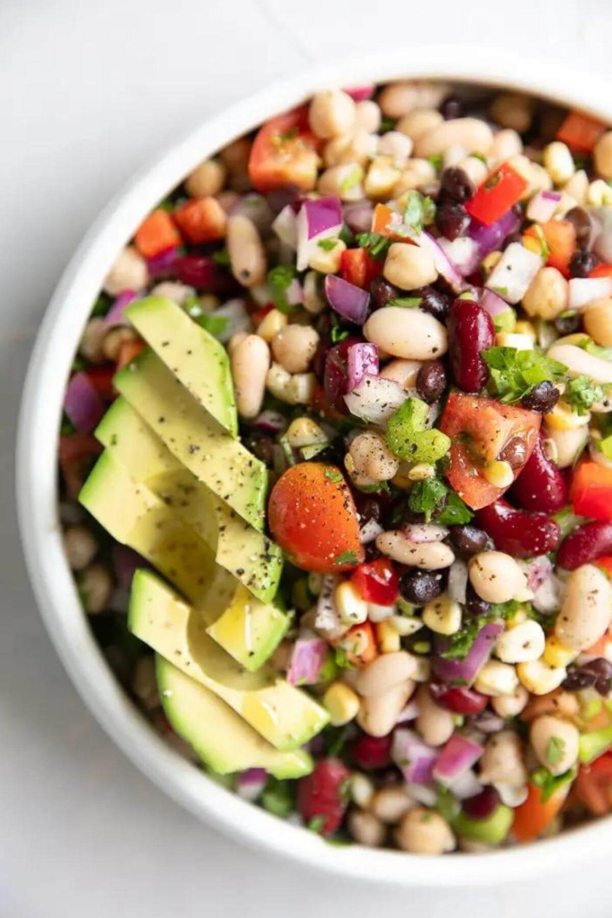 A white bean salad in a large bowl with sliced avacado.