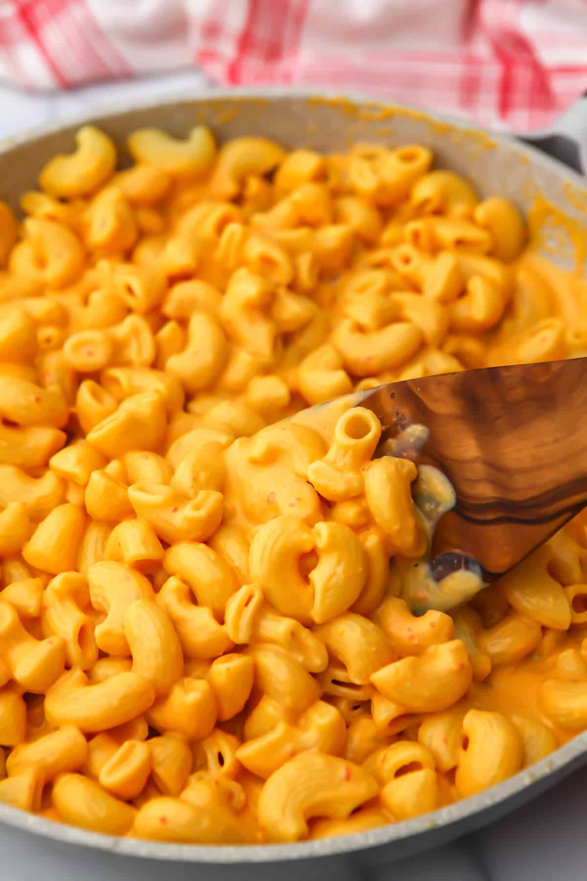 A pan of creamy tofu mac and cheese being stirred with a wooden spoon.