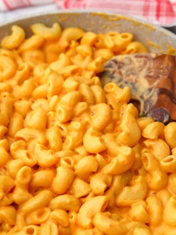 A pan full of vegan tofu mac and cheese being stirred with a wooden spoon.