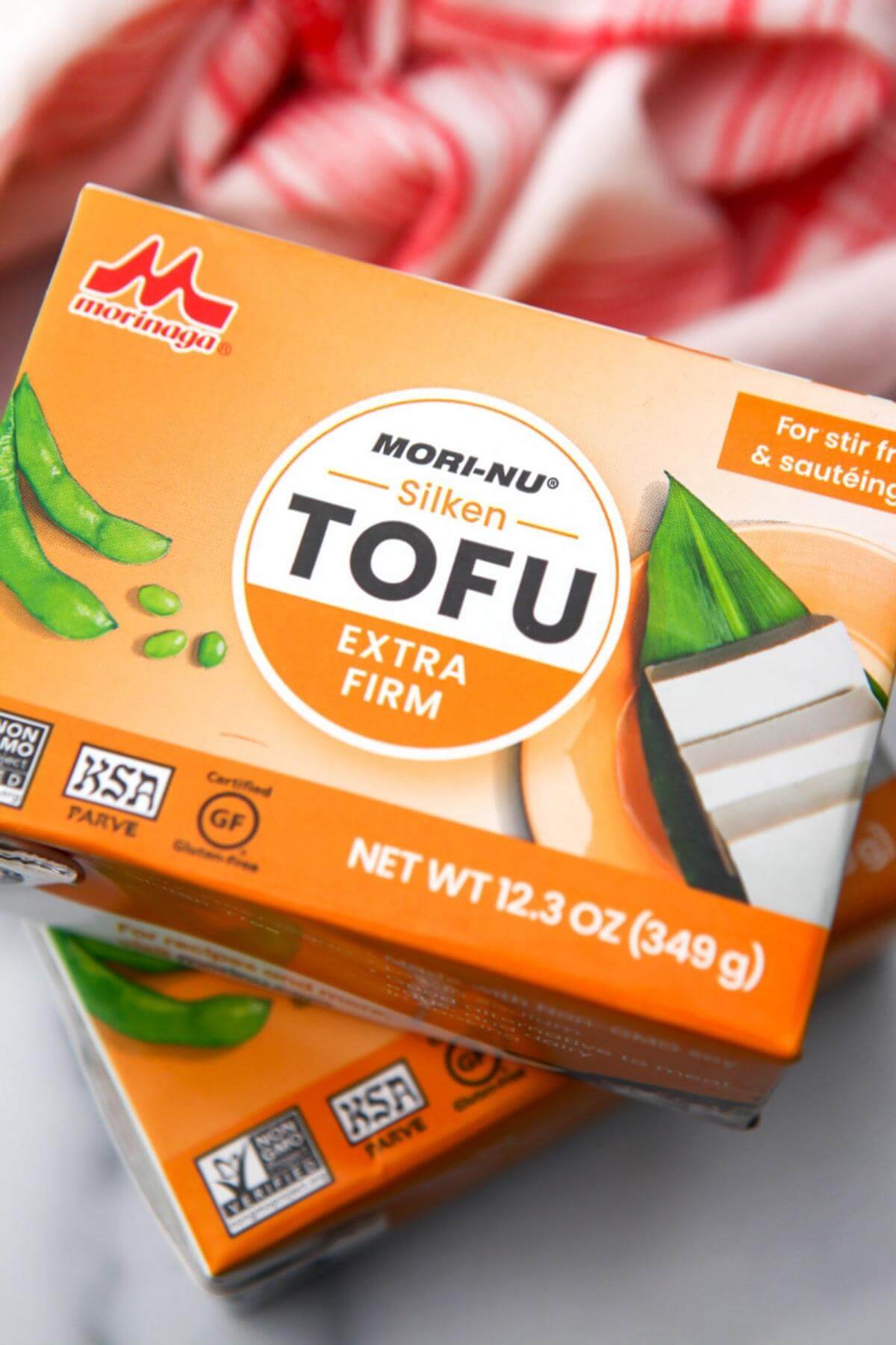 Two boxes of silken tofu on a counter top with a red tea towel behind them.