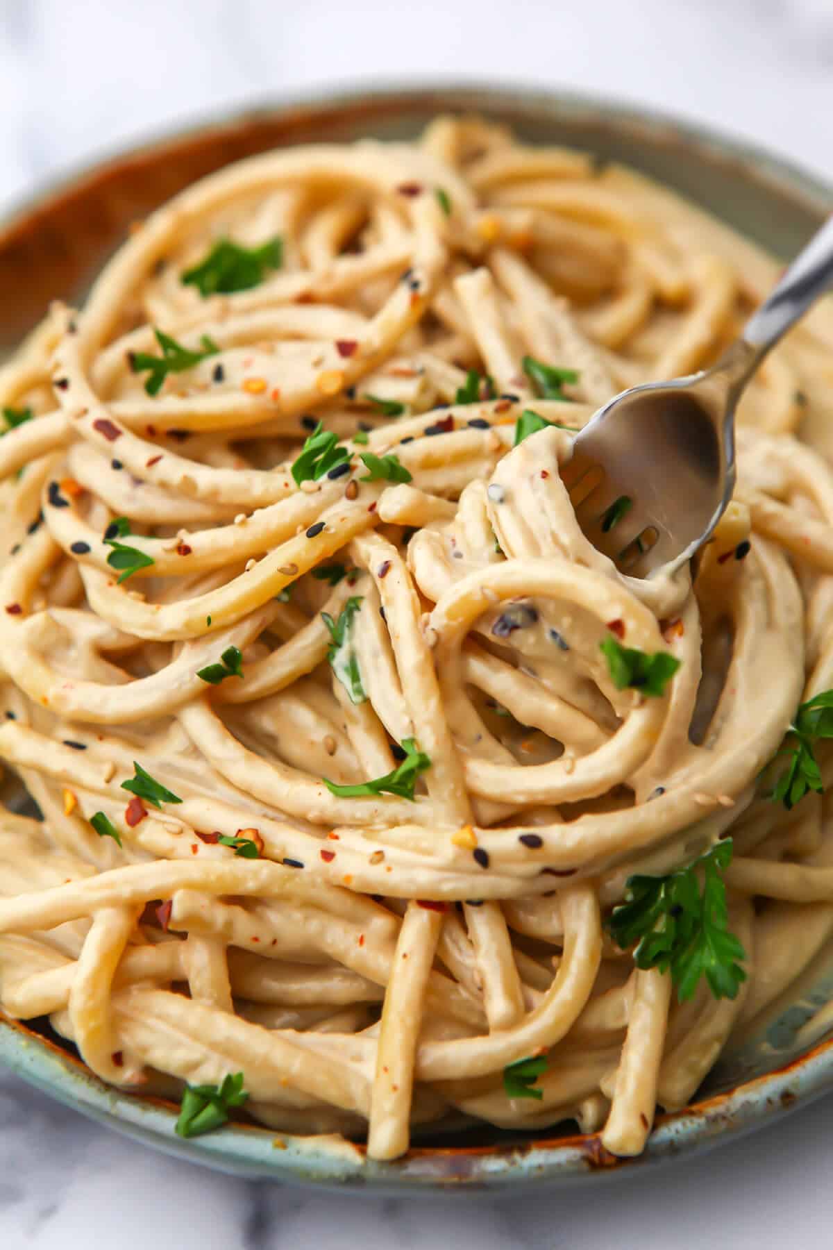 A top view of a plate full of pasta with tahini sauce on it being twirled with a fork.