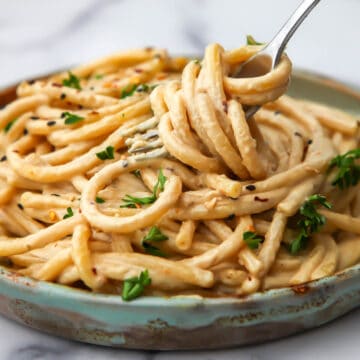 Tahini pasta with parsley on to being twirled up in a fork.