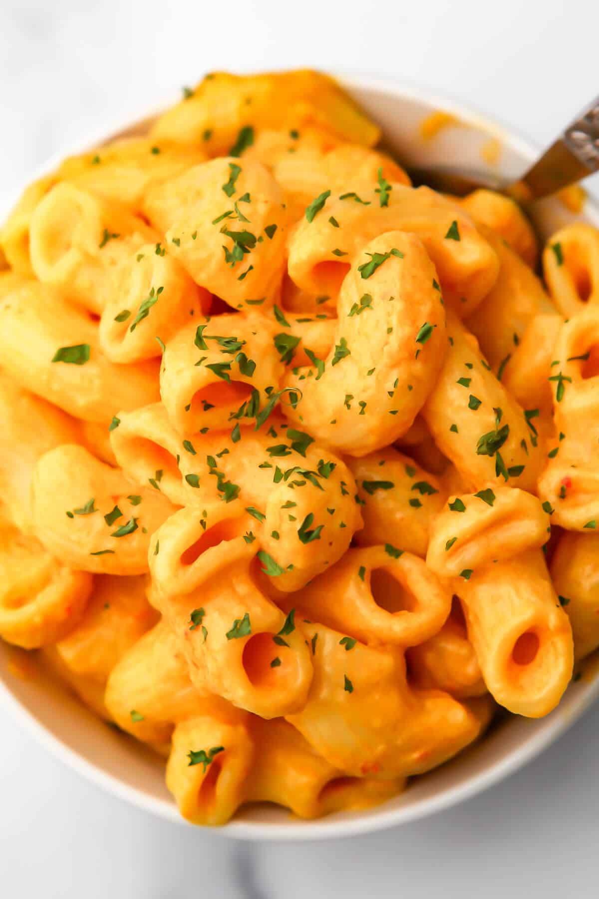 A top view of a bowl of pasta with a tofu cheese sauce with parsley sprinkled on top.