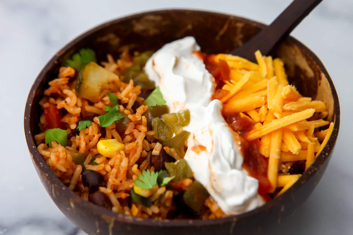 A coconut bowl filled with taco style rice with vegan cheese and sour cream for toppings.